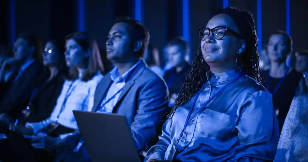 Black Female Sitting in Dark Crowded Auditorium at an International Business Conference. Multiethnic African Woman Using Laptop Computer. Delegate Watching Presentation About New Financial Solutions.
