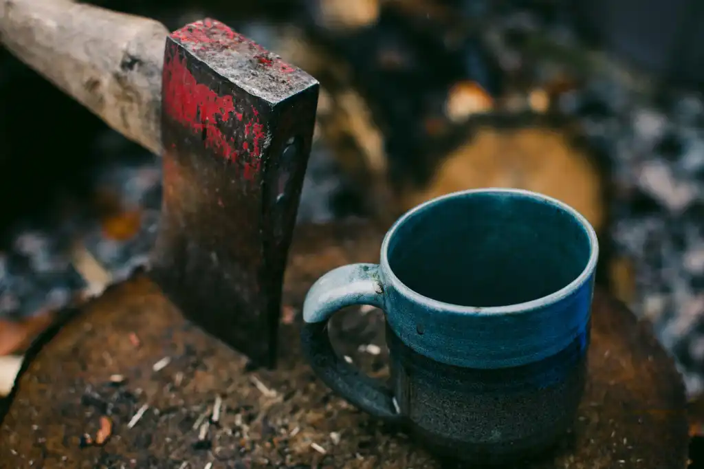Axe embedded in log next to a cup of coffee