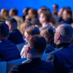 Audience sitting and attentively listening to a speaker during a business conference. The image captures a professional atmosphere with engaged participants.