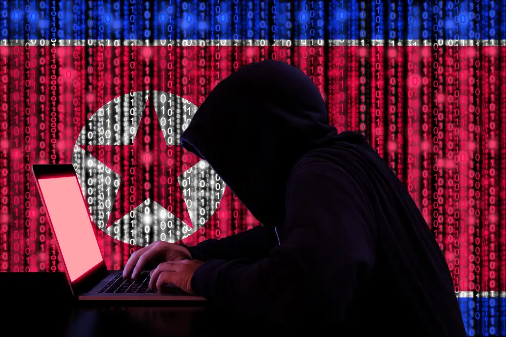 Hacker in a dark hoody sitting in front of a notebook with digital north korean flag and binary streams background cybersecurity concept