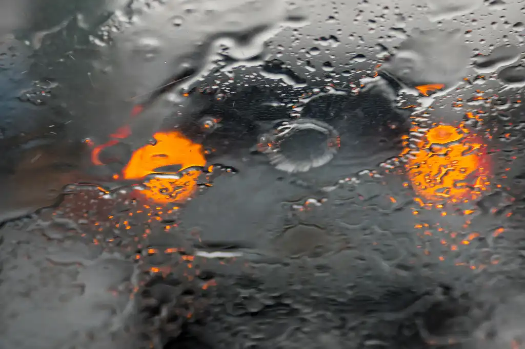 Wet glass with rain drops and silhouette of modern car