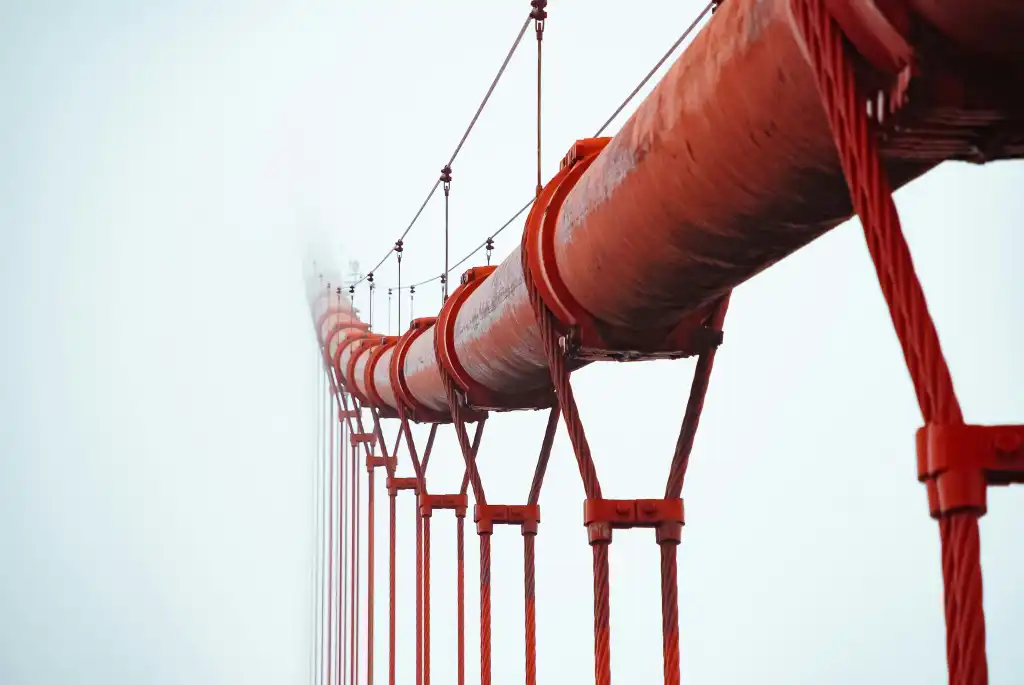 Red suspension bridge cable and vertical suspenders, representing a pipeline