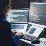 Young Asian woman, developer programmer, software engineer, IT support, wearing glasses working hard at nitght overtime on computer to check coding in bugging system. Back view