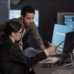 Side view portrait of two people pointing at computer screen while working in IT company