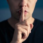 Secret and silence. Quiet silent shh gesture with finger on lips. Man doing expression with hand on mouth. Taboo topic, censorship or freedom or speech. Conspiracy theory. Confidential talk.