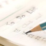 To-do list. A green pencil checking off items on a paper to-do list.