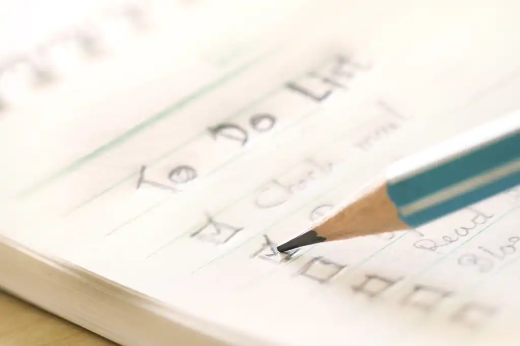 To-do list. A green pencil checking off items on a paper to-do list.