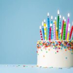 A large white birthday cake with many colorful lit candles.