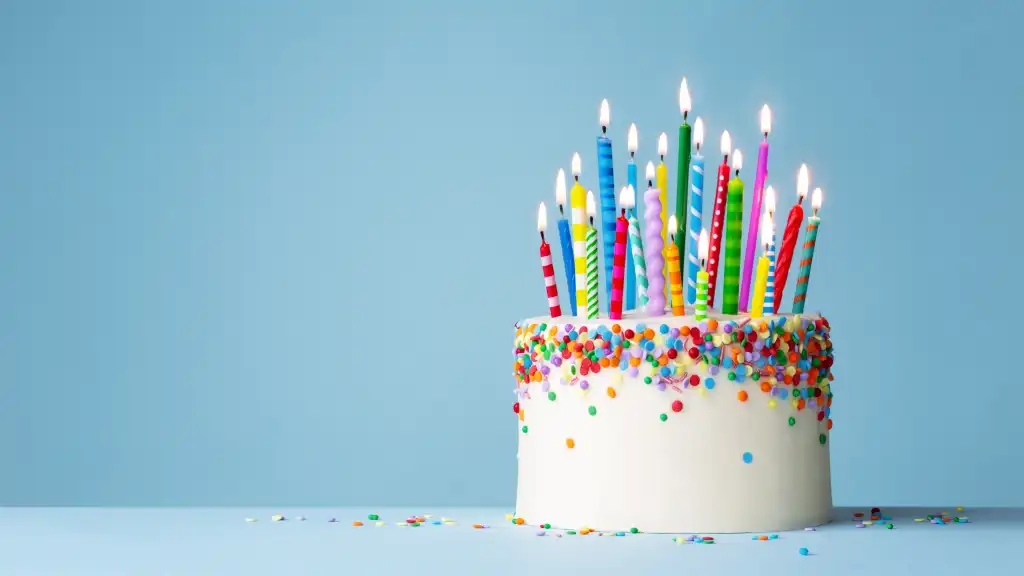 A large white birthday cake with many colorful lit candles.
