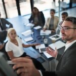 Business people, presentation and man with brainstorming, meeting and feedback with proposal. Group, employees and mentor with information, speaker and planning with teamwork, coaching and leader