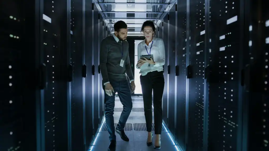 Male and Female Server Technicians Working in Data Center. Running Rack Server Diagnostics. Woman Uses Tablet Computer.