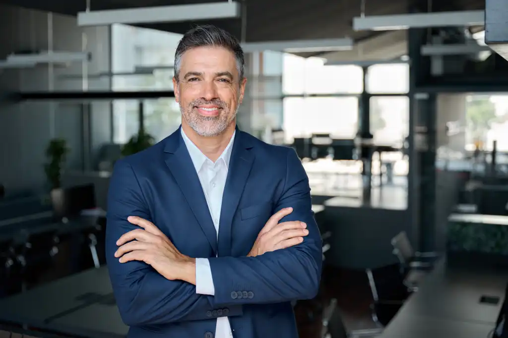 Happy middle aged business man ceo standing in office arms crossed. Smiling mature confident professional executive manager, proud lawyer, confident businessman leader wearing blue suit, portrait.