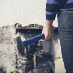 A young woman is opening up an old fireplace in a Victorian house with a sledge hammer