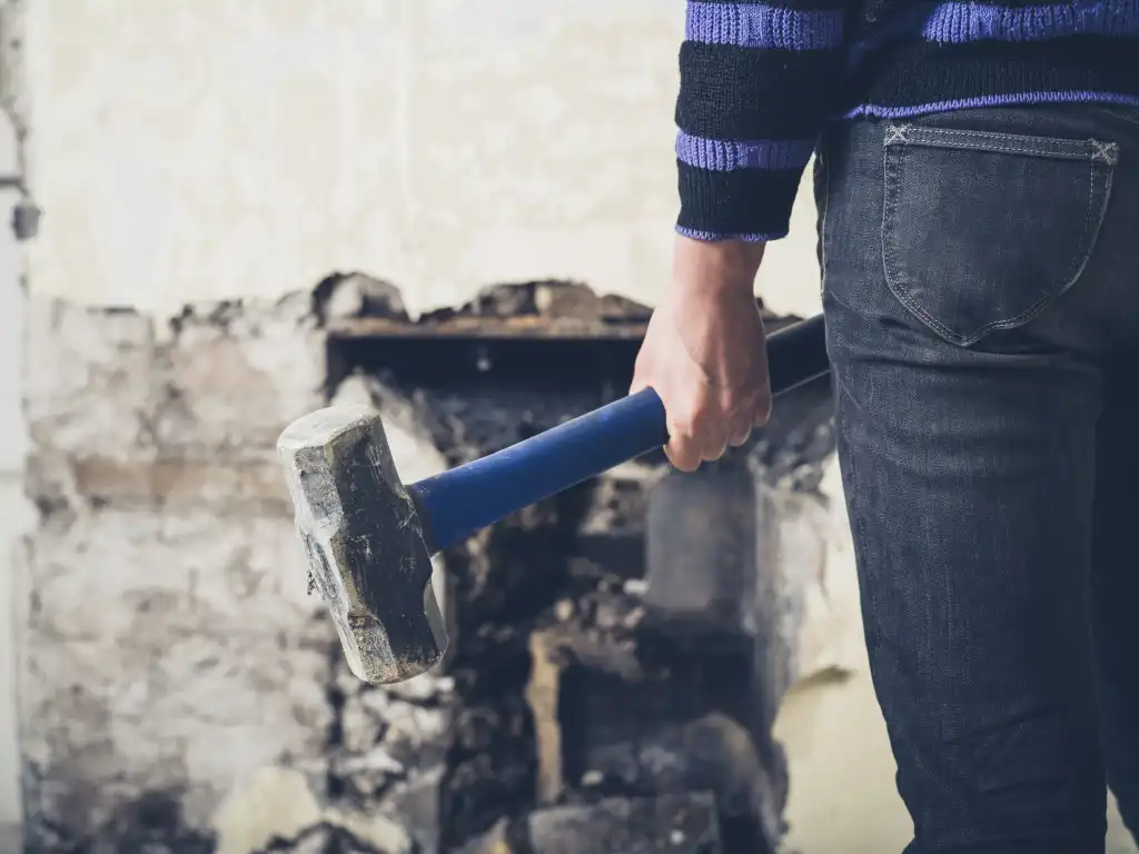 A young woman is opening up an old fireplace in a Victorian house with a sledge hammer