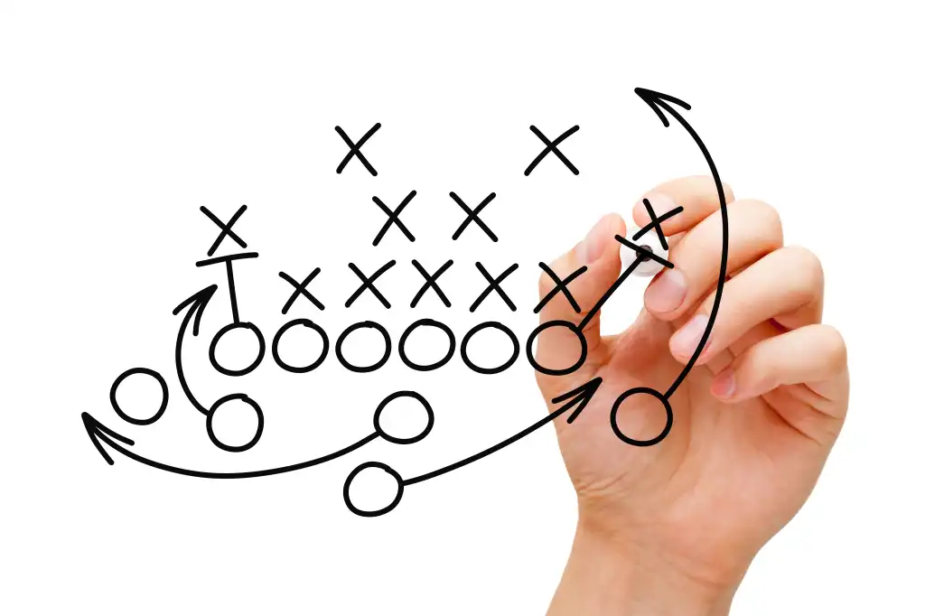A hand draws football plays on a clear screen in black marker.