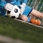 A soccer goalie stops the ball in front of the net.