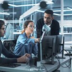 Team of Innovative Industrial Engineers Use Computer to Discuss a Technological Project in Industry 4.0 Modern Factory Office. Group of Scientists Work in Research and Development Center.