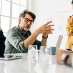 Business man explaining a project to his team. Senior business man taking the lead during a meeting. Group of business people discuss about work in an office.