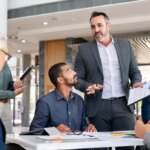 Successful entrepreneur focusing on work with charts during meeting with multiethnic employee. Mature businessman discussing work at conference table in office with senior businesswoman.