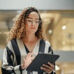 Female Data Analyst Smiling While Checking New Data for the Day. Portrait of hispanic Businesswoman Walking Towards her Business Office in a Spacious Corporate Building. Low Angle