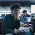 Portrait of a Thoughtful Engineer Working on Desktop Computer in a Technological Office Environment. Research and Development Department Writing Software Code for an Innovative Internet Project