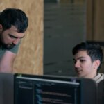 Two men working on computers in an office Code inspection with programmers