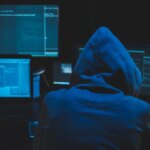 Hacker using computer for organizing massive data breach attack on goverment servers. Hacker in dark room surrounded computers