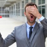 Businessman with one hand over his eyes holding a red dart. Flying blind.