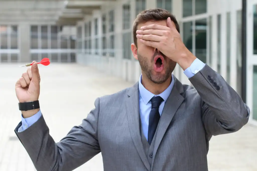 Businessman with one hand over his eyes holding a red dart. Flying blind.