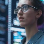 Close Up Portrait of Woman Working on Computer, Lines of Code Language Reflecting on her Glasses from Big Display Screens. Female Programmer Developing New Software, Coding, Managing Cybersecurity