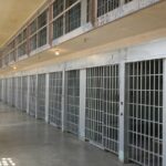 A picture of a hallway full of prison cells.