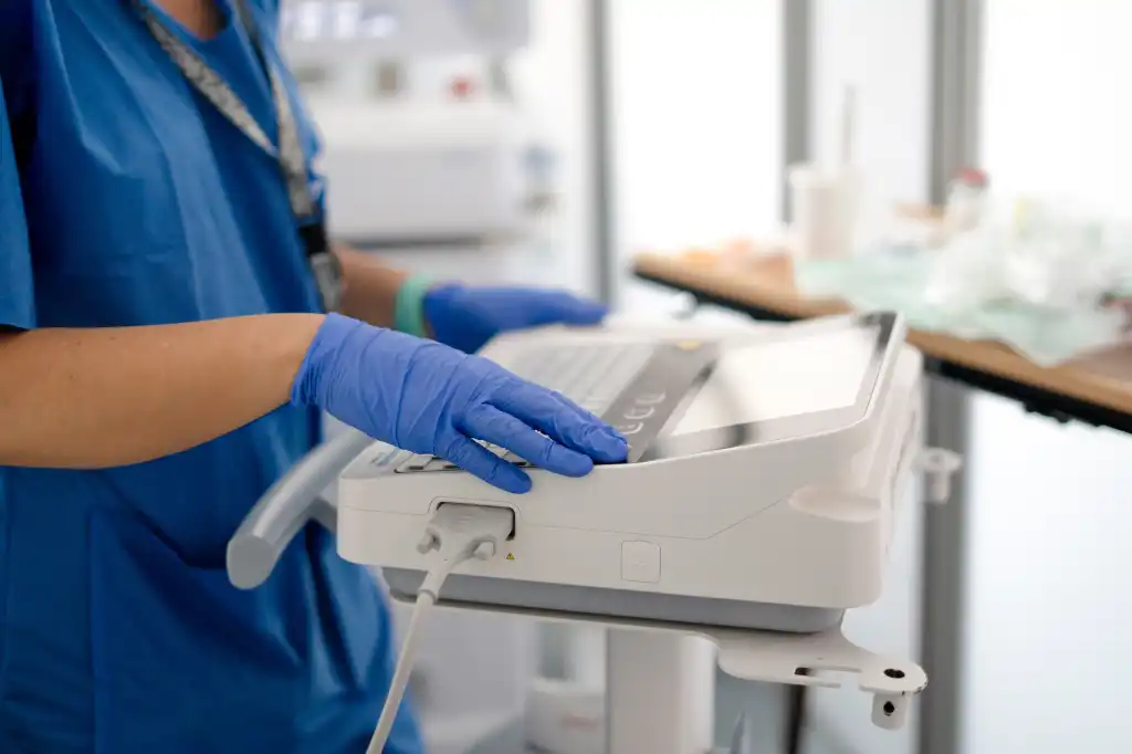 Healthcare worker wearing blue scrubs and gloves operating a medical ultrasound device