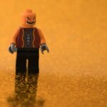 a pumpkin head lego figure is standing on a shiny orange surface
