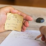 Man using formula math sheet to cheat on test. Hand of university student holding pencil doing math question in examination and cheating with answer piece of paper in hand