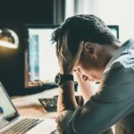 Tired and worried business man at workplace in office holding his head on hands after late night work, concept
