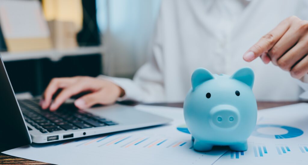 A picture of a person on a computer putting money in a piggy bank