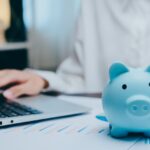 A picture of a person on a computer putting money in a piggy bank